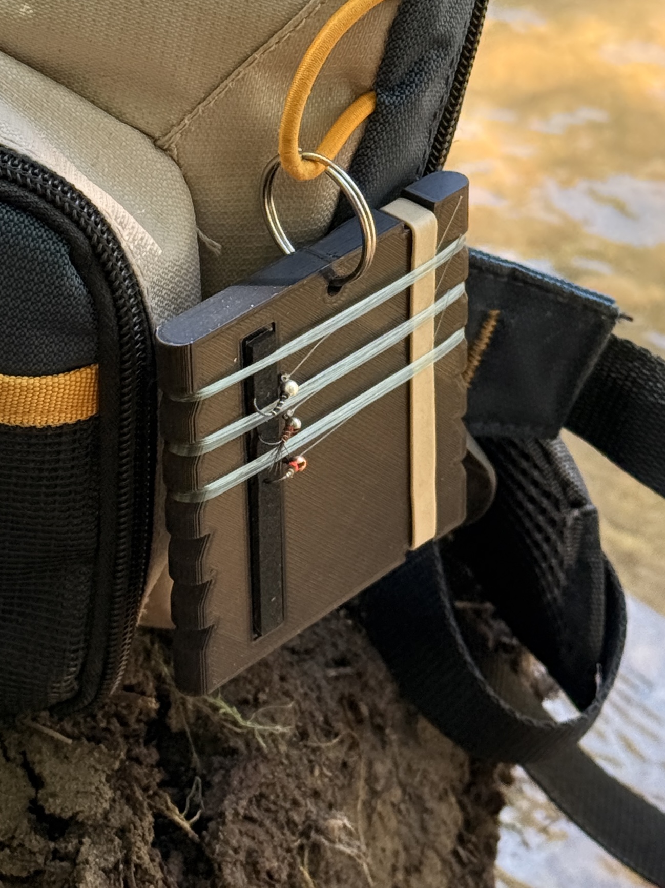 Tired Leader leader-storage disc clipped to a fishing pack streamside, rigged with leader and flies